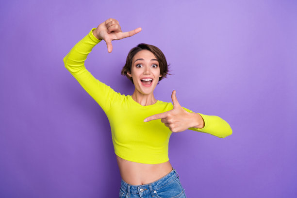 有趣的年轻女孩穿着时尚的夏季服装，惊讶地用手指做出框架，拍摄照片，背景为紫色。图片下载