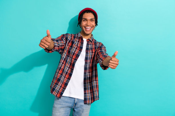 帅气年轻男子的照片肖像，双手竖起大拇指，穿着时尚的格子服装，背景为青色。图片下载