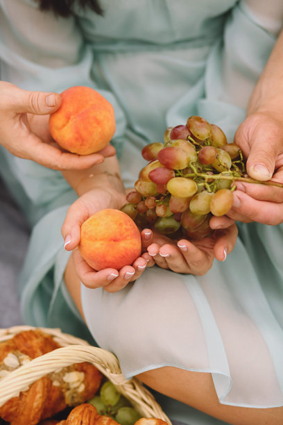 人们在户外休息时手中拿着桃子和葡萄的特写照片。家庭在大自然中享受野餐午餐。图片下载