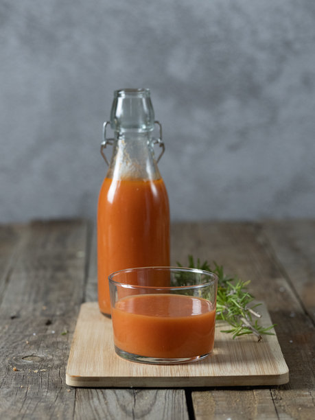 垂直照片：一个盛有冷汤的玻璃杯，背景中有一瓶，放在托盘上，背景为木质纹理。图片下载