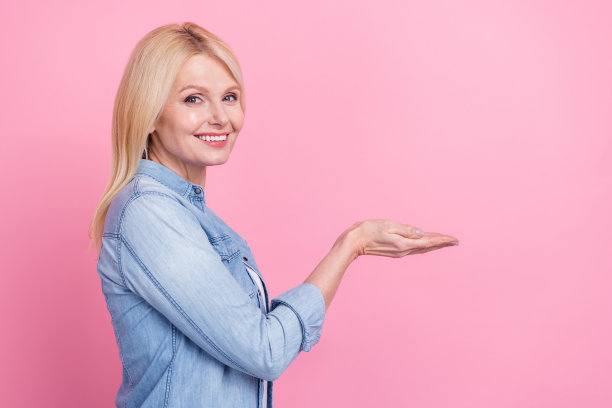 迷人的老年女士在粉色背景下双臂张开，手持慈善捐款横幅，展示产品尺寸的个人资料照片图片下载