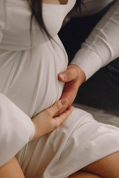 孕妇穿着白色裙子，和丈夫手握着孕肚的特写照片。爱的概念。图片下载