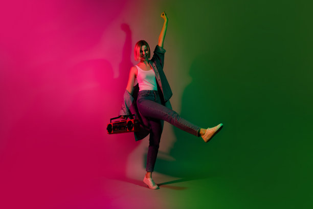 充满活力的年轻女性在多彩的霓虹色背景下，手持音响尽情狂欢的全身照片图片下载