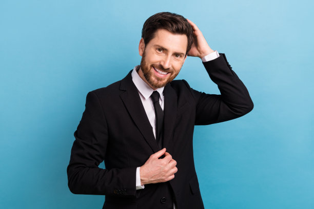 穿着黑色礼服的快乐迷人男经理在蓝色背景下整理发型的照片图片下载