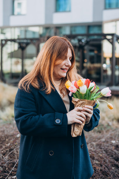 美丽的年轻女性手捧春天的郁金香花束，走在城市街道上。快乐的女孩在户外摆姿势。春季背景下的漂亮女性肖像。高质量照片。图片下载