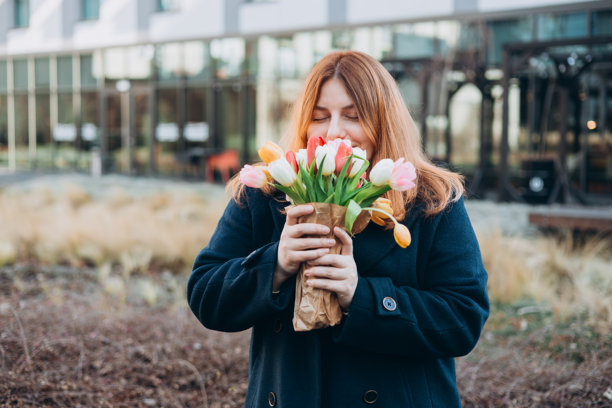 美丽的年轻女性手捧春天的郁金香花束，在城市街道上漫步。快乐的女孩在户外摆姿势。春季背景下的漂亮女性肖像。高质量照片。图片下载