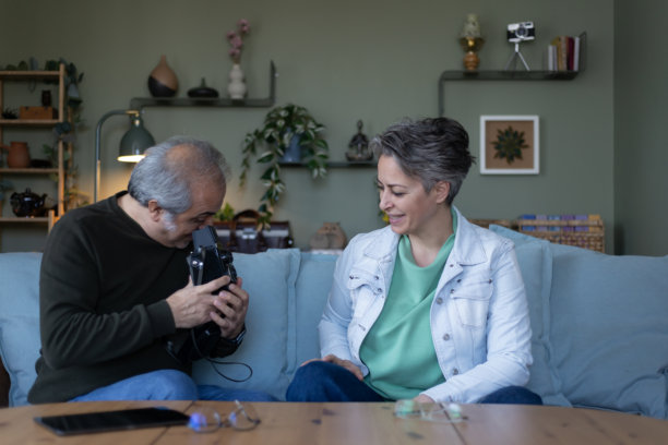 两个退休老人坐在沙发上研究一台复古相机。他们准备拍几张照片。图片下载