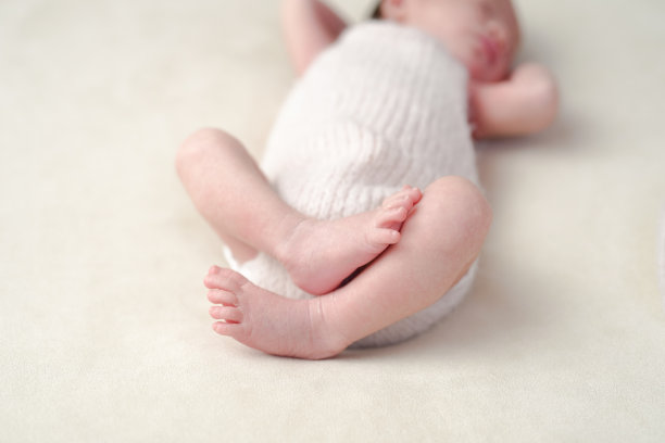 一名7天大的日本新生儿在白色背景上安静地睡着，穿着柔软的粉色连体衣。这张温柔的照片突显了宝宝甜美的表情和早期婴儿期的宁静魅力。图片下载