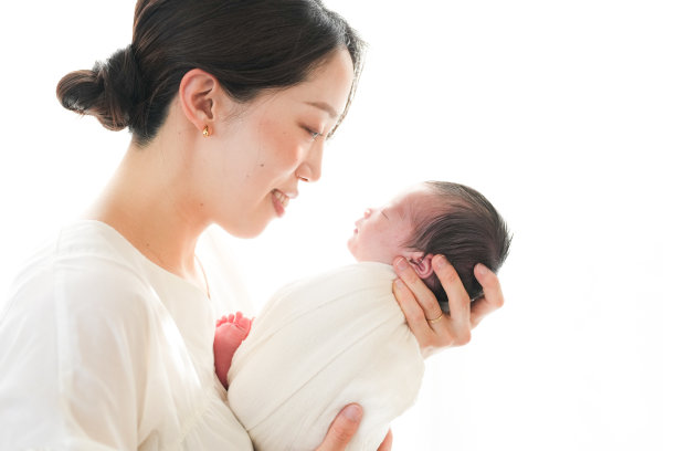 一位二十多岁的母亲抱着她七天大的日本新生儿，背景为白色。这张照片捕捉了母子之间温暖、爱与亲密的联系。图片下载