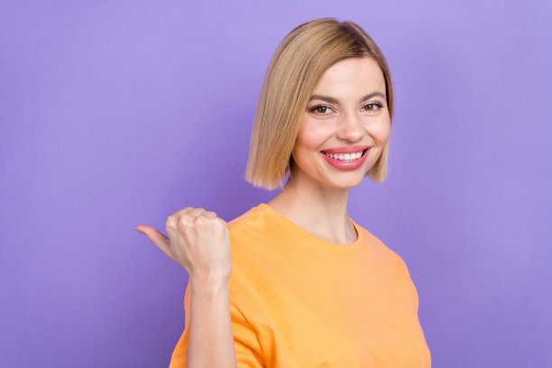 年轻女性推广员的照片肖像，手指指向空白广告空间，穿着T恤，背景为紫色。图片下载