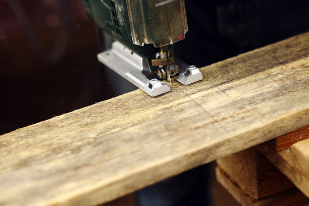 户外工作的木匠使用曲线锯。特写照片显示男子正在用曲线锯切割木块。文本留白空间。图片下载