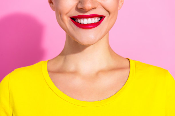 特写剪裁的照片，展现了微笑的女士，露出洁白的牙齿，涂着红色口红，背景为粉色。图片下载