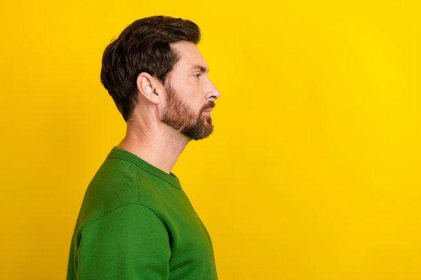 自信的商人侧面照片，棕色胡须和深色头发，吸引人的外表，望向空白空间，背景为黄色。图片下载