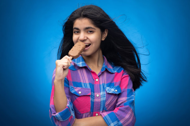 青少年女孩在蓝色背景下吃巧克力冰淇淋的肖像照片图片下载