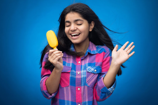 青少年女孩在蓝色背景下吃芒果冰淇淋的肖像照片图片下载