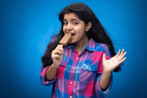 青少年女孩在蓝色背景下吃巧克力冰淇淋的肖像照片图片下载