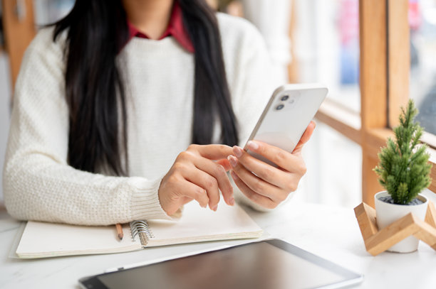 特写镜头：一位女性的手握着手机，正在点击屏幕。坐在咖啡馆的桌子旁。图片下载