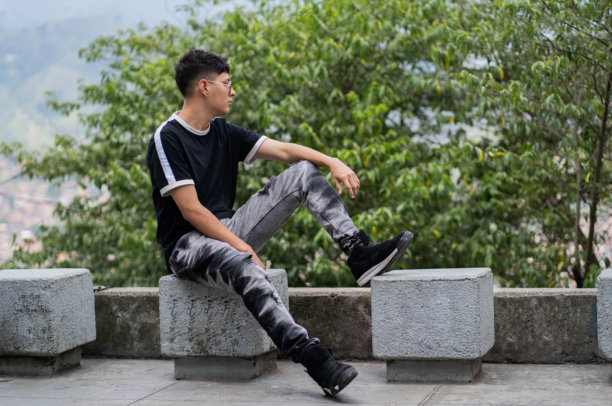 现代年轻男子坐在城市环境中的户外，周围环绕着自然 - 休闲随意风格 - 股票照片图片下载