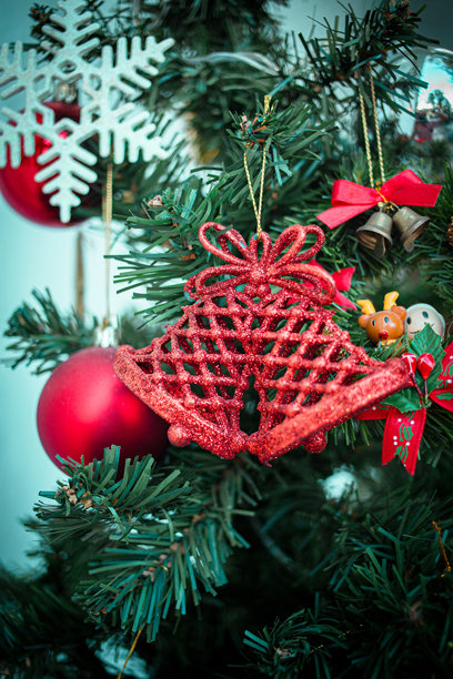 闪亮的红色铃铛装饰品优雅地悬挂在闪烁着节日魅力的绿色冷杉树枝上，展现出圣诞装饰的优雅。竖版照片图片下载
