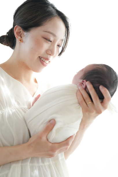 一位二十多岁的母亲抱着她七天大的日本新生儿，背景为白色。这张照片捕捉了母子之间的温暖、爱与亲密的联系。图片下载