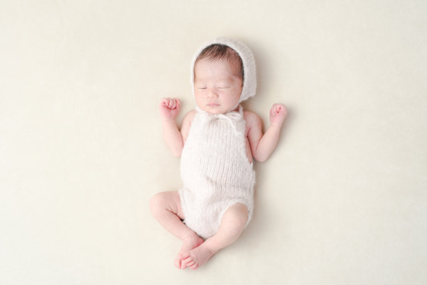 一名7天大的日本新生儿在白色背景上安静地睡着，穿着柔软的粉色连体衣和配套的帽子。这张温馨的照片捕捉了早期婴儿的细腻魅力和宁静。图片下载