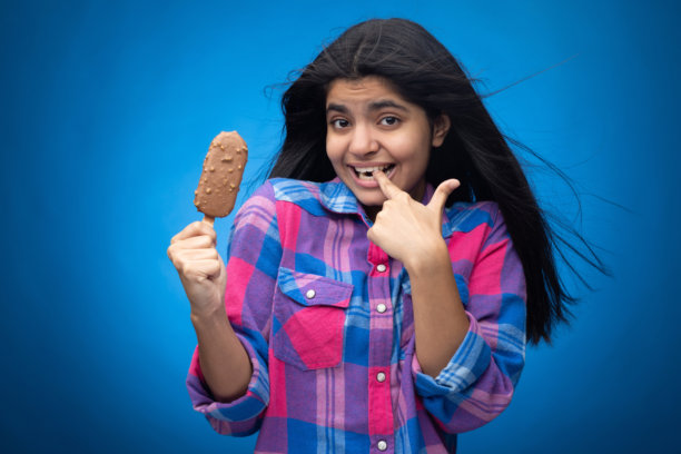 青少年女孩在蓝色背景下吃巧克力冰淇淋的肖像照片图片下载