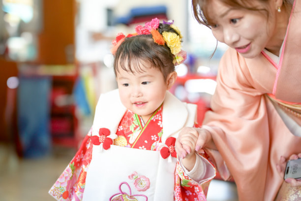 一位穿着红色和服的3岁日本女孩和她母亲穿着粉色和服，在美容院为七五三做准备。这张照片捕捉了她们在特别日子到来之前的宁静亲密关系。图片下载