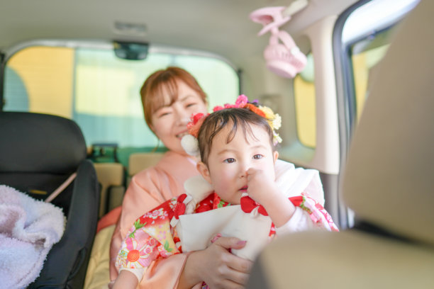 一位穿着红色和服的三岁日本女孩和她母亲穿着粉色和服，坐在车里，前往七五三庆祝活动。这张图片捕捉了她们在这个特殊日子里的安静兴奋。图片下载