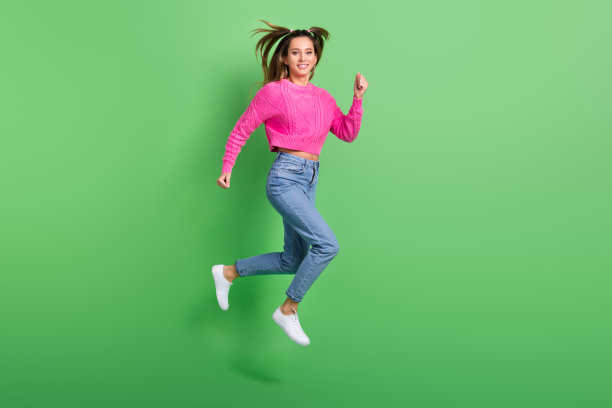 穿着粉色毛衣和牛仔裤的美丽可爱女性在绿色背景上飞奔赶往特卖会的全身照片图片下载