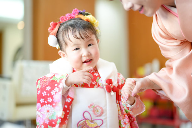 一位穿着红色和服的3岁日本女孩和她的母亲穿着粉色和服，在美容院为七五三做准备。这张照片捕捉了她们在特别日子到来之前的宁静亲密关系。图片下载