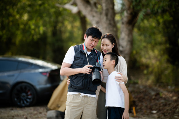母亲和儿子正在看父亲用相机拍的照片。家庭旅行，去露营。图片下载