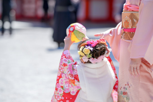 一个穿着红色和服的三岁日本女孩在庆祝七五三。她和穿着粉色和服的妈妈一起玩纸气球玩具。这张照片捕捉了母女之间甜美的瞬间。图片下载