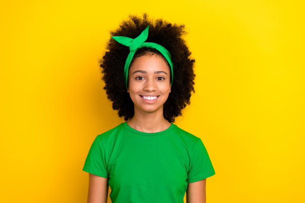 穿着绿色T恤、戴着发带的可爱女士在黄色背景下微笑，照片光亮。图片下载