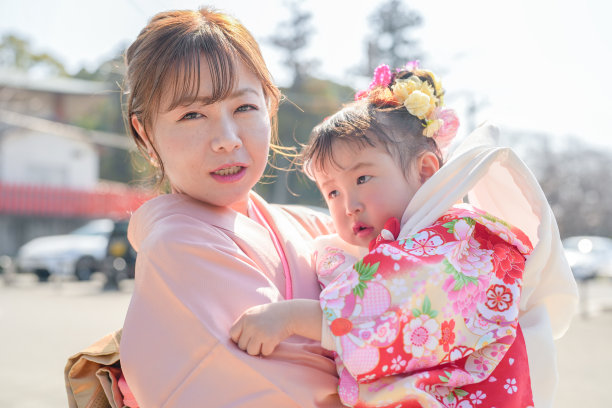 一个穿着红色和服的三岁日本女孩与她的父母（妈妈穿着粉色和服，爸爸穿着西装）在停车场庆祝七五三节。这张图片捕捉了温馨的家庭时刻。图片下载
