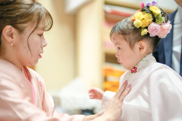 一对三十多岁的日本夫妇，穿着粉色和服，正在帮助他们三岁的女儿穿上她的和服，准备庆祝七五三。这张照片捕捉了家庭的爱与关怀，展现了传统庆典前的温馨时刻。图片下载