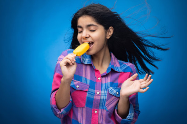 青少年女孩在蓝色背景下吃芒果冰淇淋的肖像照片图片下载