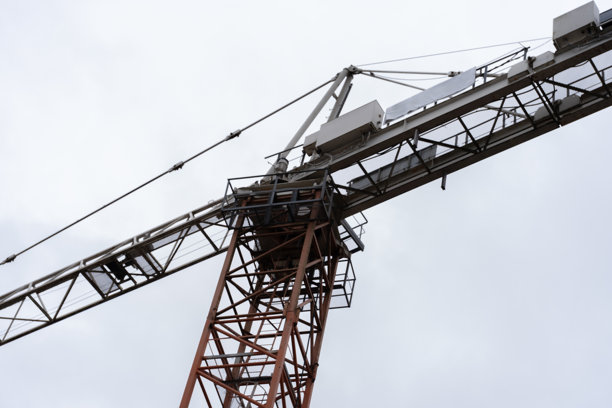 一座高耸的建筑起重机在淡色天空下的细节视图。照片强调了起重机的几何结构，展示了其复杂的设计和工业用途。图片下载