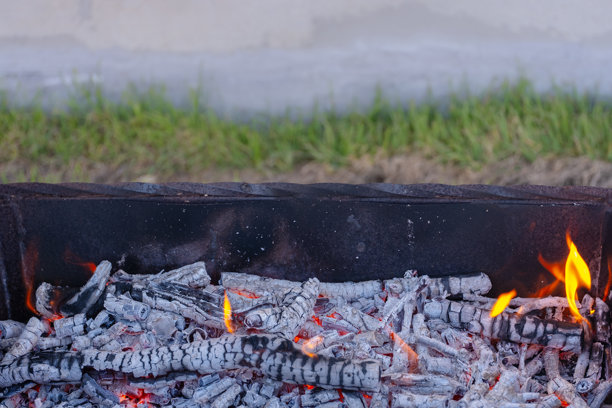 烧烤架中发光的炭火特写，间隙中闪烁着小火焰。炽热的煤炭散发着热量，使这张图片非常适合展示户外烹饪和烧烤。图片下载