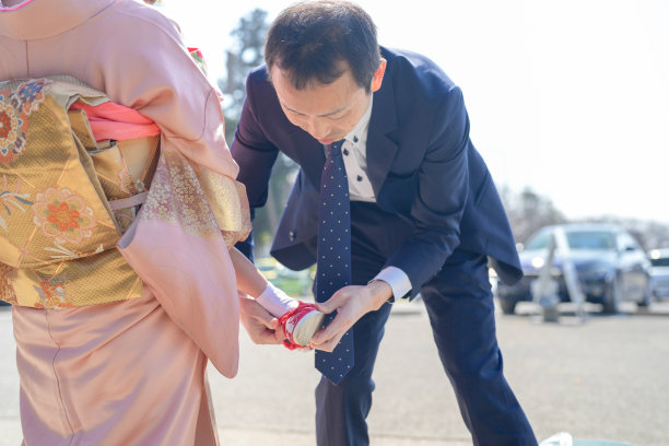 一个穿着红色和服的三岁日本女孩在停车场与她的父母站在一起——妈妈穿着粉色和服，爸爸穿着西装——庆祝七五三节。这张图片捕捉了温馨的家庭时刻。图片下载