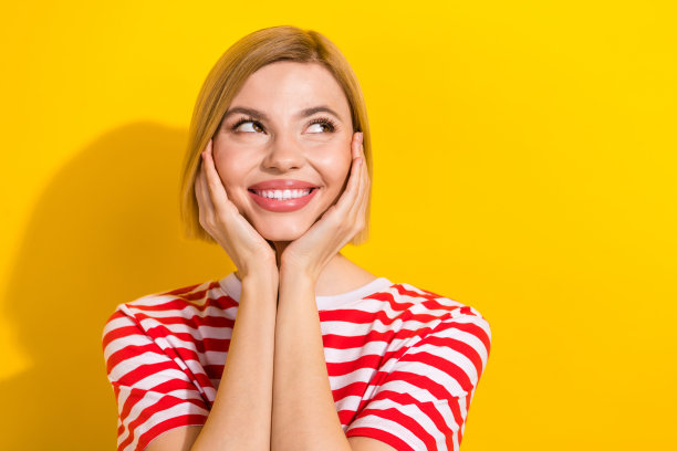 特写照片，漂亮满意的女孩穿着时尚的夏季服装，双手触碰脸庞，仰望空旷的空间，背景为黄色。图片下载