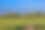 这张照片展示了一个风景，前景是绿色的田野，接着是一座有树木的山丘和一栋红屋顶的白色建筑。画面的上方是蓝天。图片下载