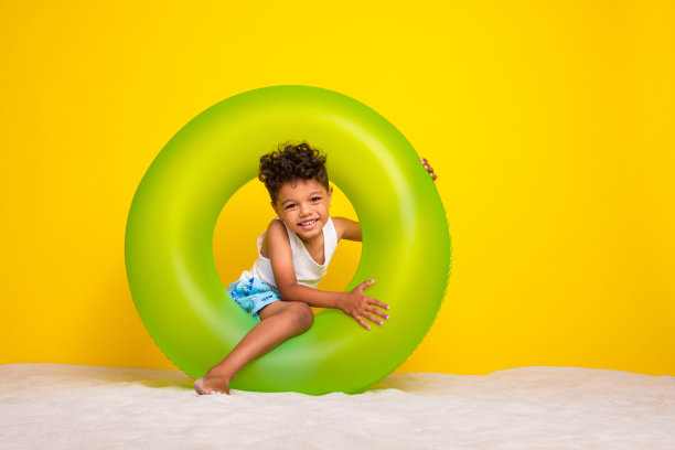 穿着白衬衫的活泼小男孩在黄色背景下享受漂浮圈的乐趣，照片为全身照。图片下载