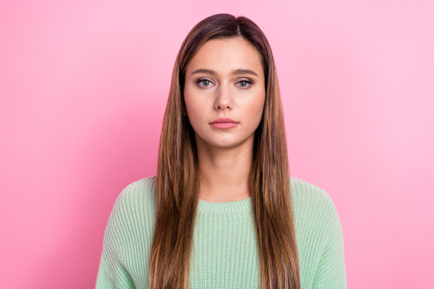 可爱年轻女孩的肖像照片，面带自信而严肃的表情，穿着绿色时尚毛衣，脸庞可爱，背景为粉色。图片下载