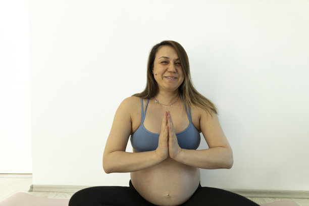 安静快乐的孕妇在室内练习瑜伽冥想，特写手与孕肚的照片图片下载