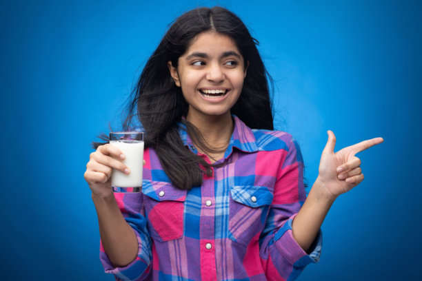 年轻女孩在蓝色背景下喝牛奶的肖像照片图片下载