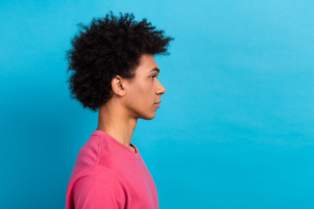 侧面照片，展现了一位穿着时尚T恤的好心人，留着卷发，注视着空旷的空间，背景为蓝色。图片下载