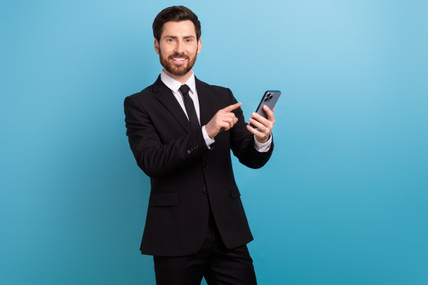 穿着黑色西装的快乐招聘者指着苹果三星现代设备的照片，背景为蓝色。图片下载