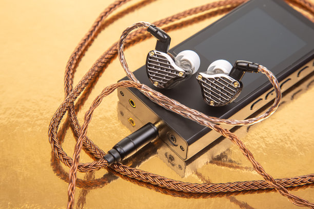 一对带编织线缆的有线耳塞放在黑色音频设备上，背景为金色。非常适合科技、音乐和音频设备主题。高分辨率库存照片。图片下载