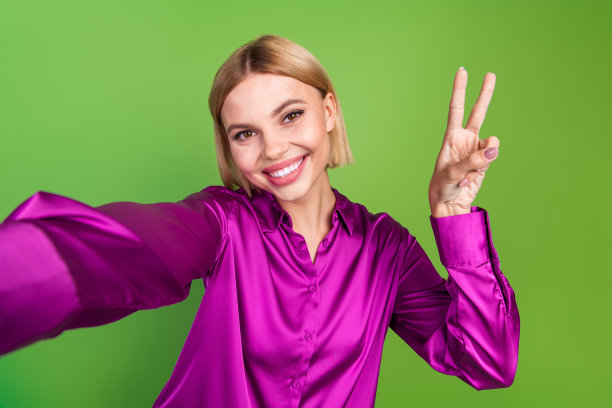 穿着时尚粉色衣服的快乐可爱女孩在绿色背景上做V字手势的照片图片下载