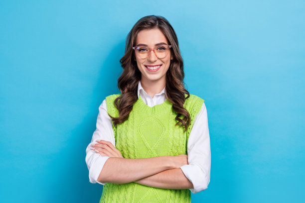 穿着时尚绿色服装的年轻女孩，戴着眼镜，双臂交叉，专业员工，蓝色背景下的照片肖像。图片下载